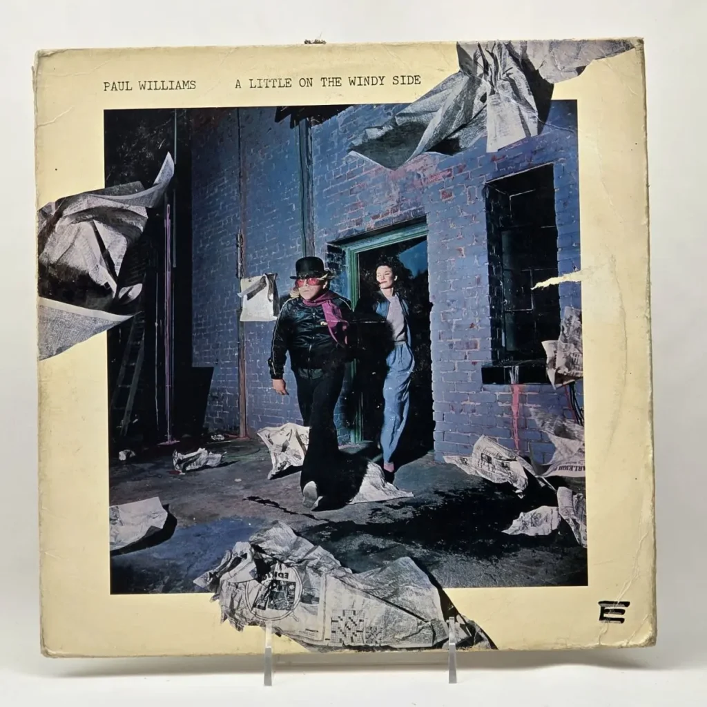 Paul Williams - A Little on the Windy Side portada del álbum, con un hombre y una mujer saliendo de un edificio con periódicos volando. by Remates Narvaja