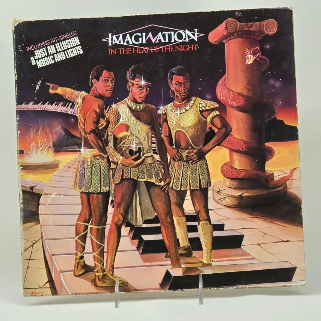 Portada del álbum Imagination - In the Heat of the Night con tres miembros de la banda vestidos de guerreros dorados, una serpiente en una columna by Remates Narvaja