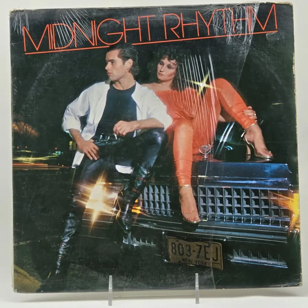Portada de álbum disco "Midnight Rhythm" con hombre en cuero y mujer en naranja sobre un coche de noche. by Remates Narvaja