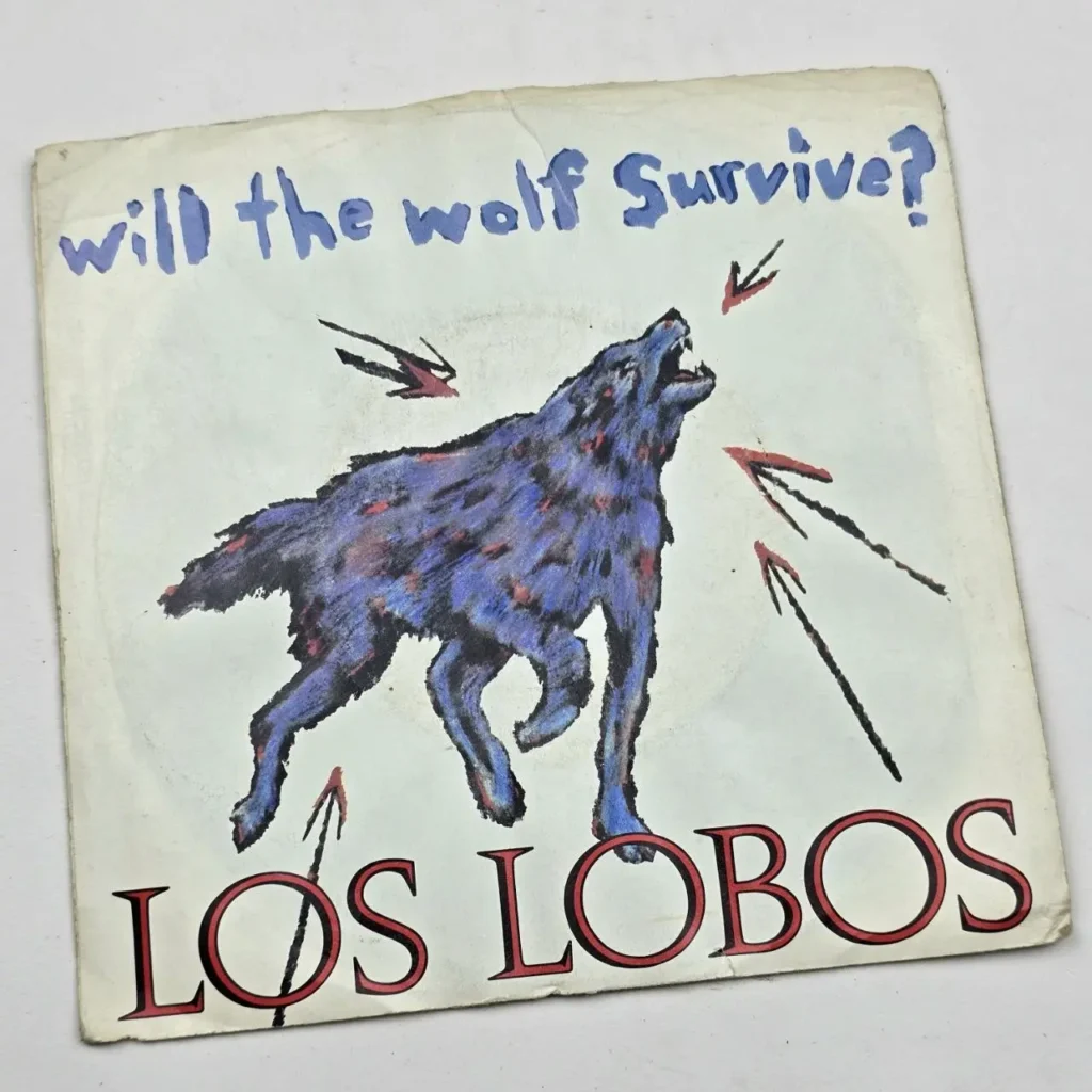 Portada del single 'Will the Wolf Survive?' de Los Lobos, con un lobo azul aullando y flechas rojas." by Remates Narvaja