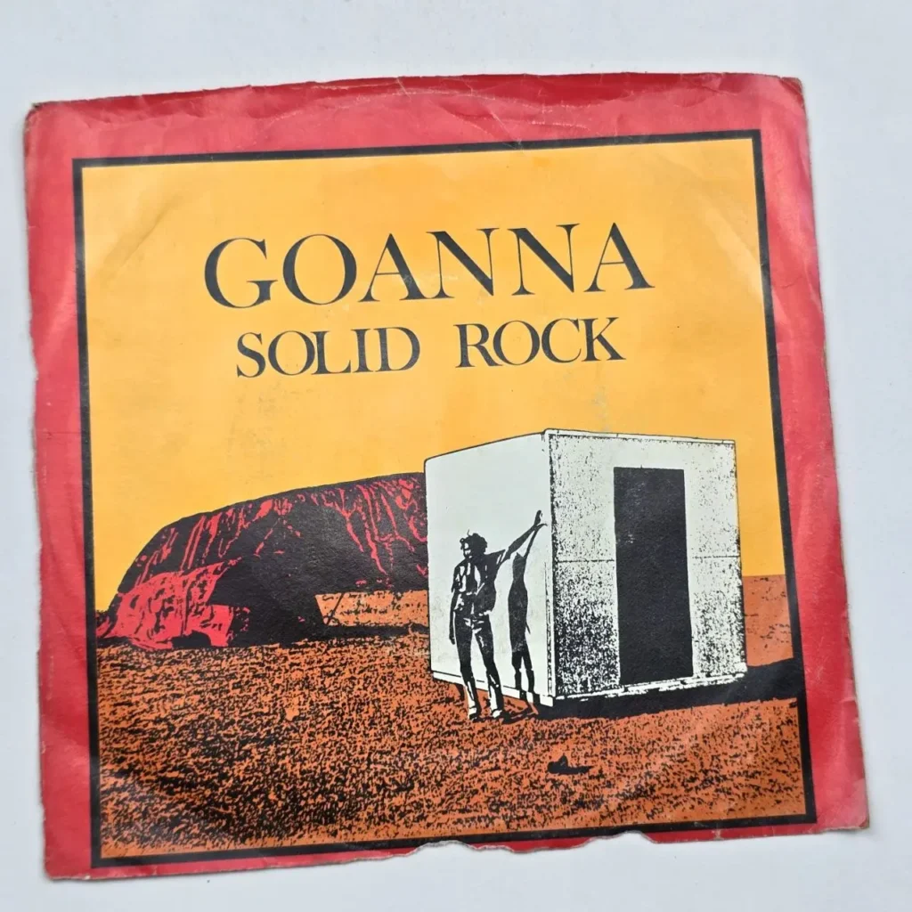 Portada del single "Solid Rock" de Goanna, mostrando Uluru, un paisaje desértico y una figura junto a una estructura blanca. by Remates Narvaja