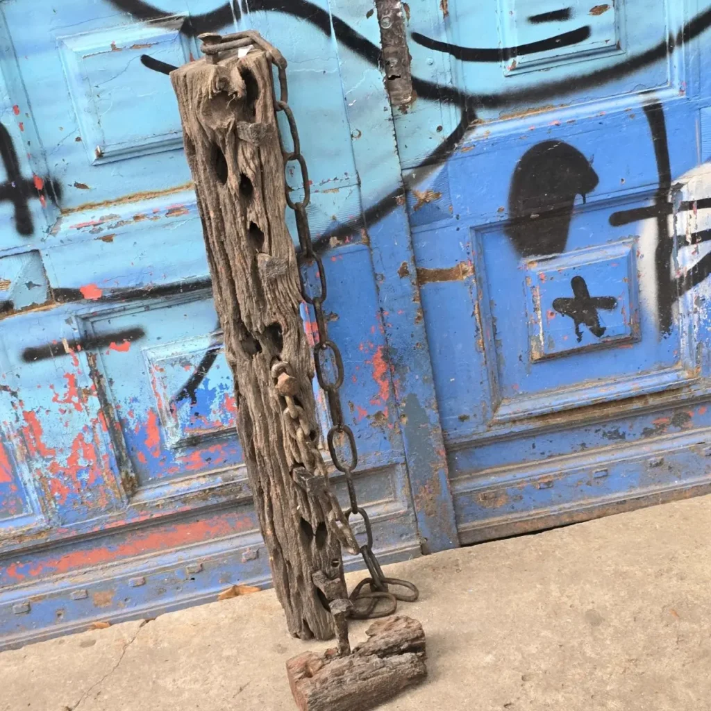Poste de madera rústico con cadena frente a puerta azul desgastada y con graffiti. by Remates Narvaja
