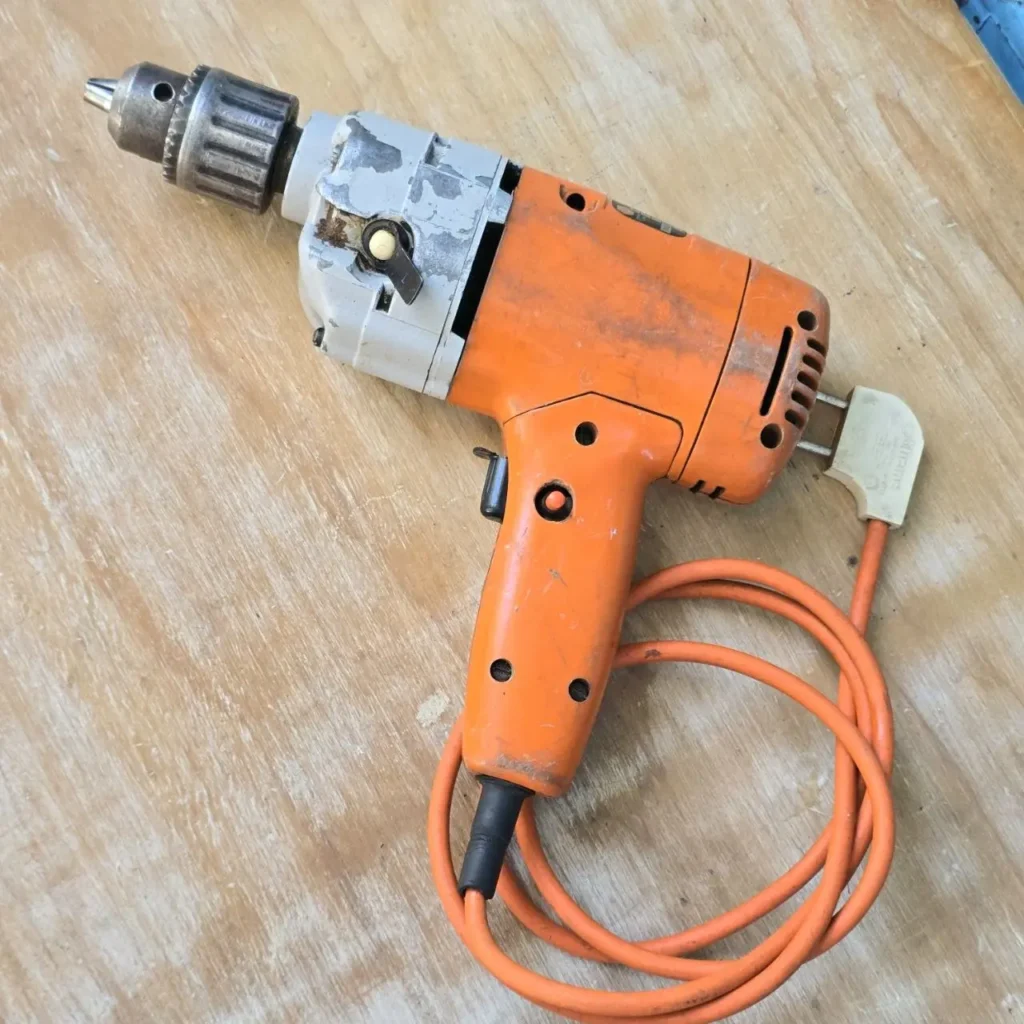 Taladro eléctrico naranja usado con su cable enrollado sobre una superficie de madera. by Remates Narvaja