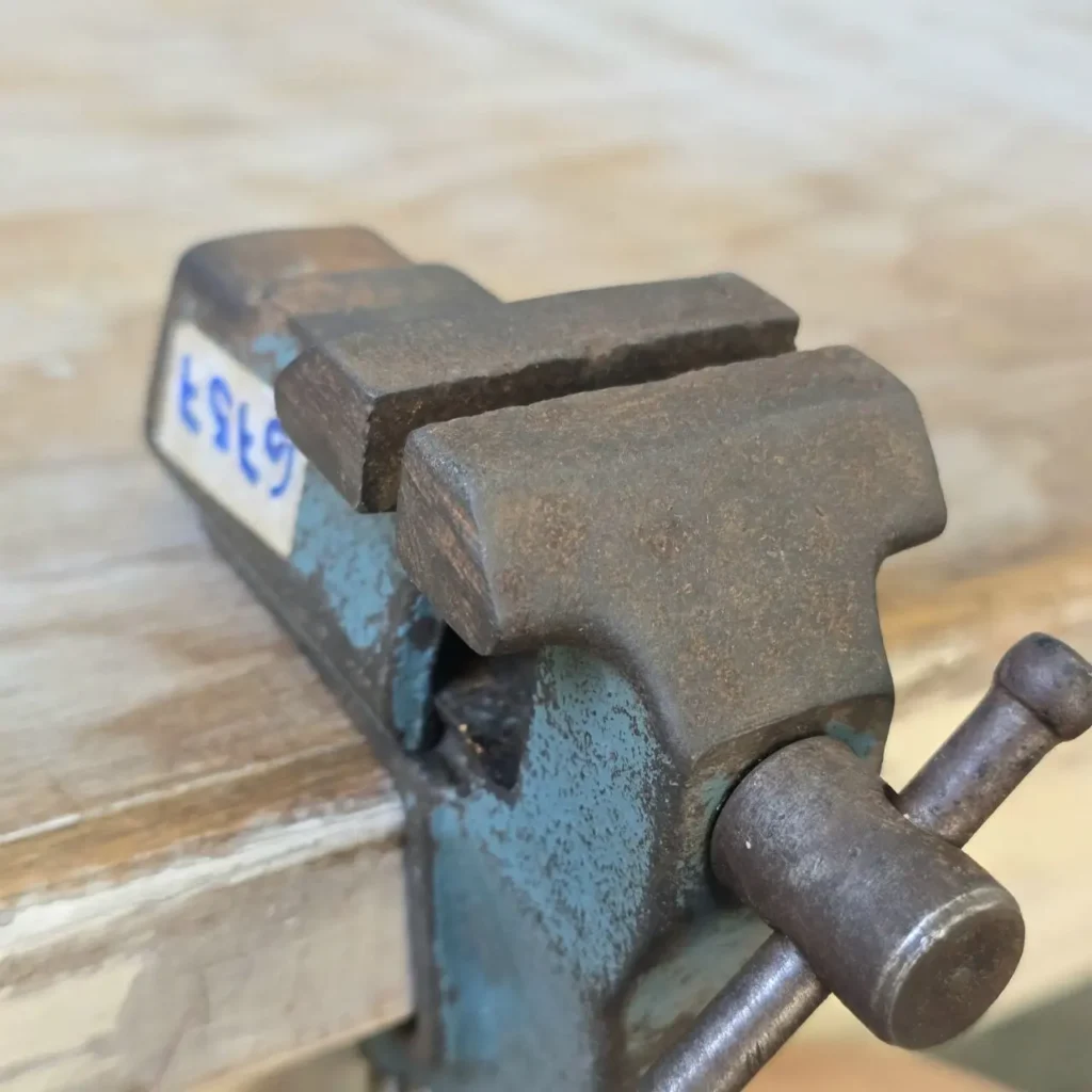 Tornillo de banco de metal azul oxidado sujetado a una mesa de madera. by Remates Narvaja