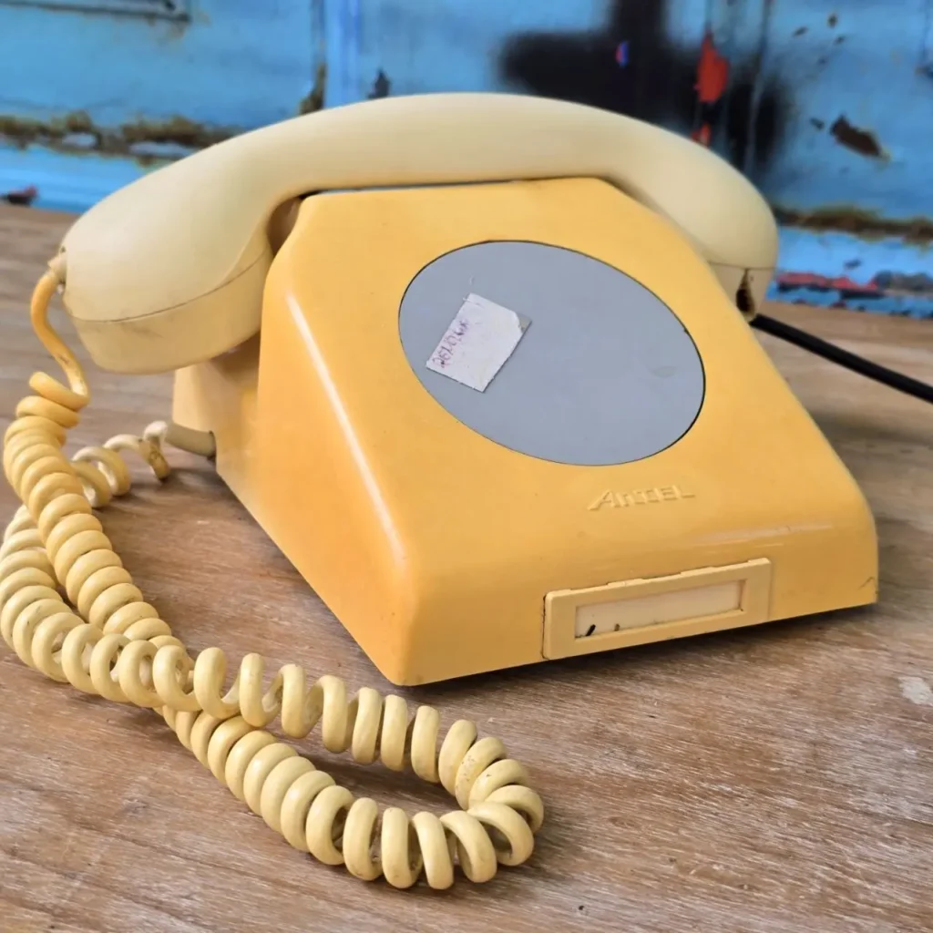 Teléfono antiguo amarillo Artel con cable en espiral sobre madera. by Remates Narvaja
