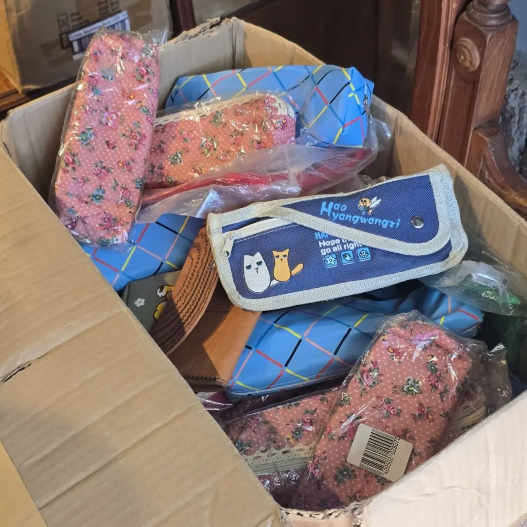 Caja de cartón llena de estuches y bolsas pequeñas, algunas con estampado floral rosa y otras azules con diseño de gatos. by Remates Narvaja