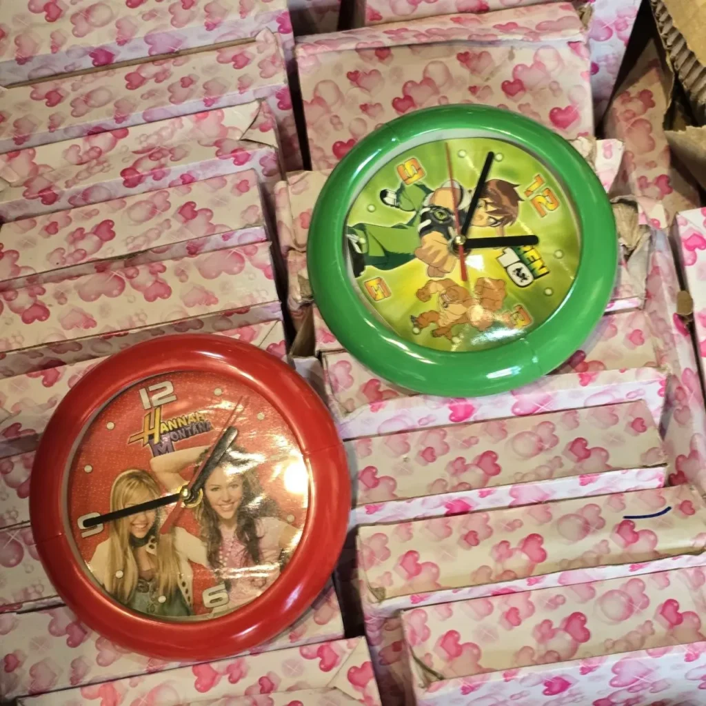 Dos relojes infantiles: uno rojo de Hannah Montana y uno verde de Ben 10, sobre cajas con patrón de corazones rosados. by Remates Narvaja