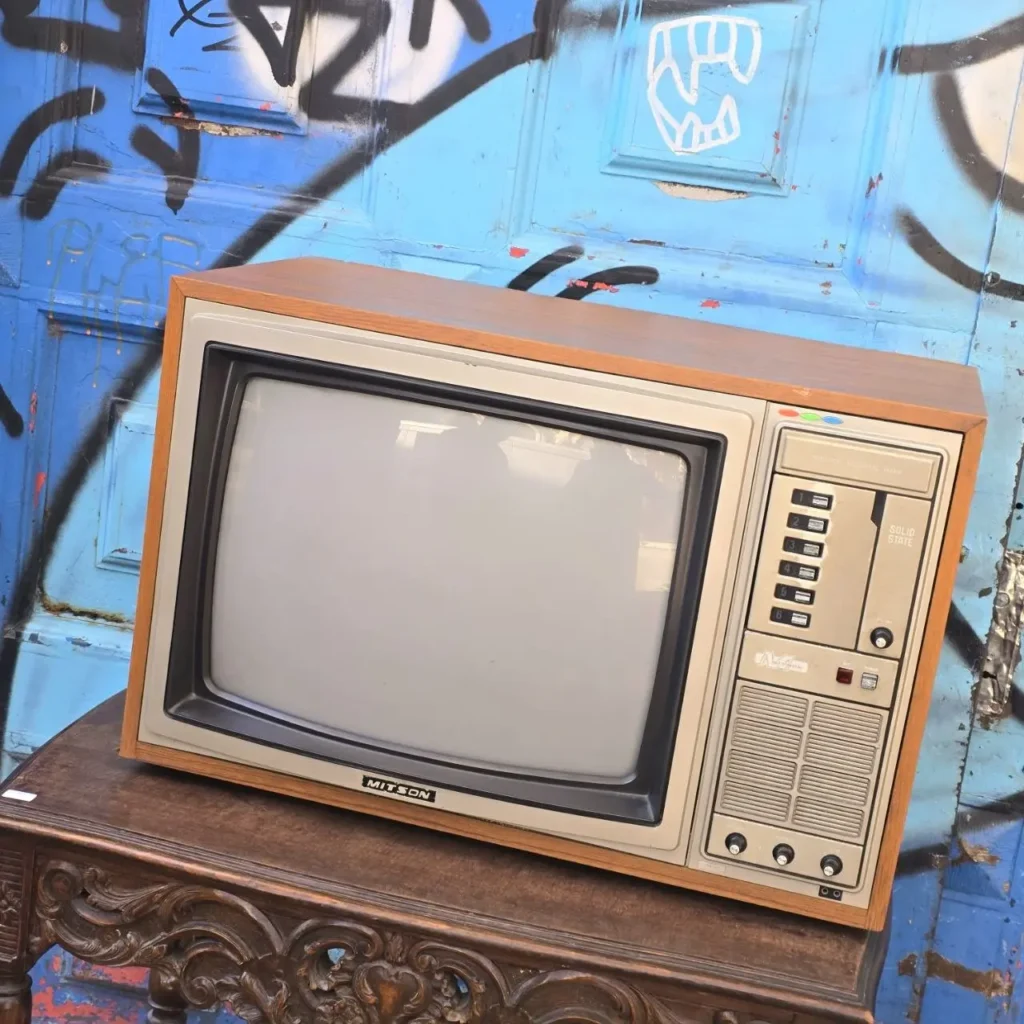 Televisor retro MITSON con carcasa de madera sobre mesa, fondo de graffiti azul. by Remates Narvaja