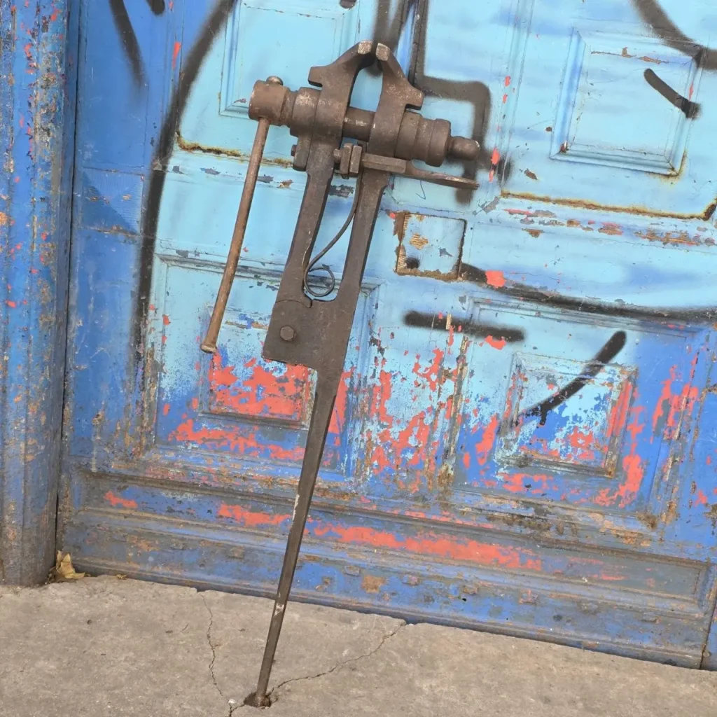 Torno de herrero antiguo y oxidado apoyado en una puerta azul descascarada con grafiti. by Remates Narvaja