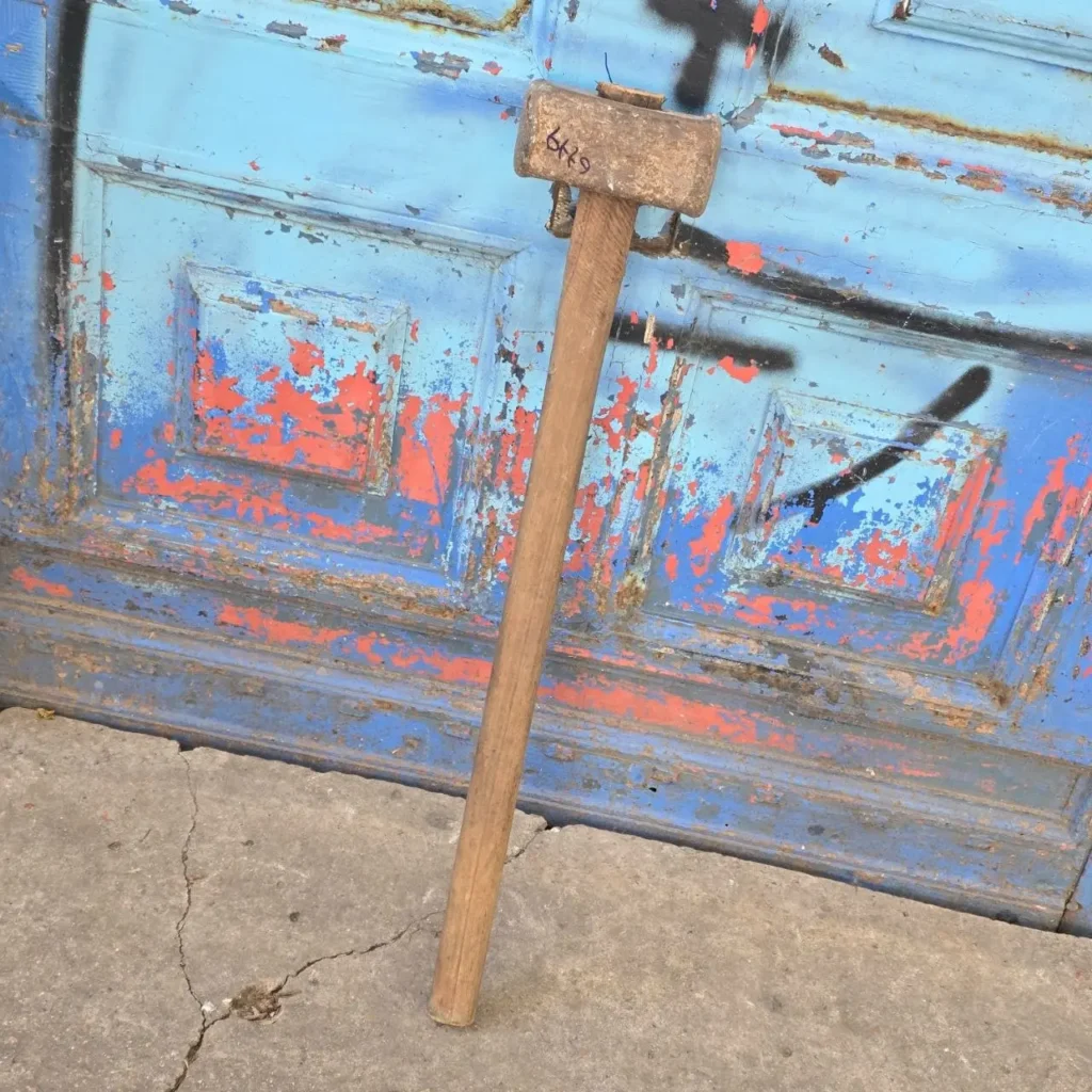 Mazo de madera y metal apoyado en puerta azul descascarada con graffiti. by Remates Narvaja