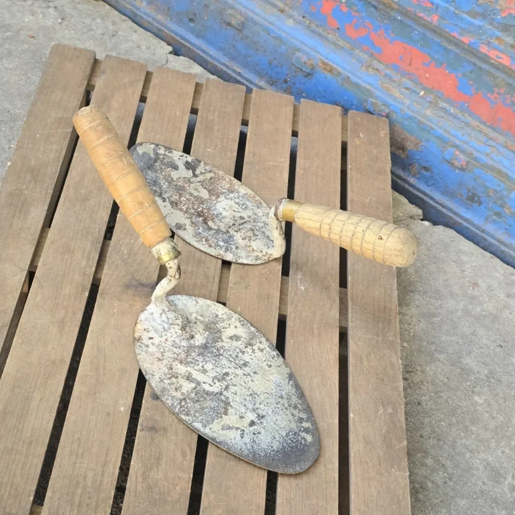 Dos paletas de albañil viejas y oxidadas con mangos de madera sobre una superficie de madera. by Remates Narvaja
