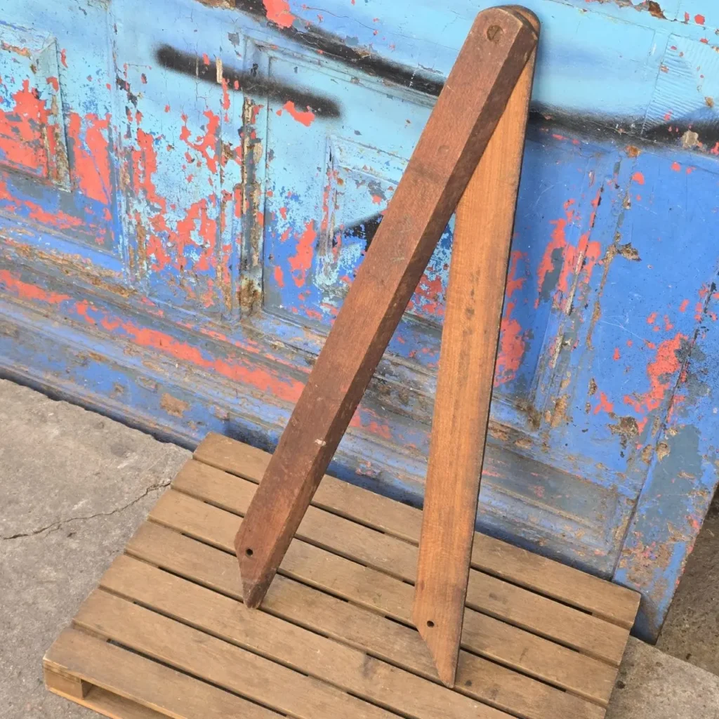 Dos listones de madera rústicos apoyados contra una puerta azul y roja con pintura descascarada, sobre un palet de madera. by Remates Narvaja