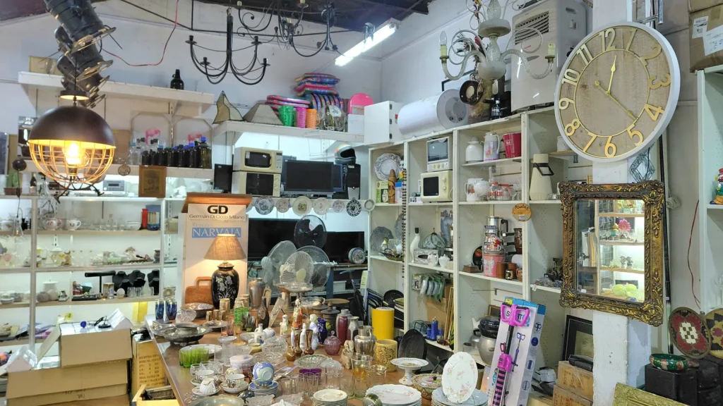 Tienda de segunda mano con variedad de artículos para el hogar, vajilla, electrodomésticos, lámparas y un gran reloj de pared. by Remates Narvaja