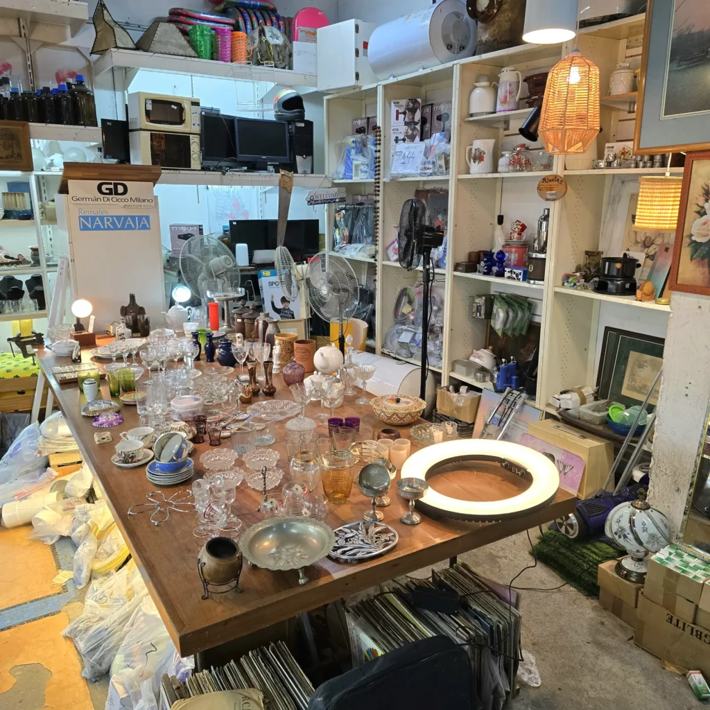 Tienda de remates Narvaja con mesa de cristalería y estantes de artículos para el hogar y electrónicos. by Remates Narvaja