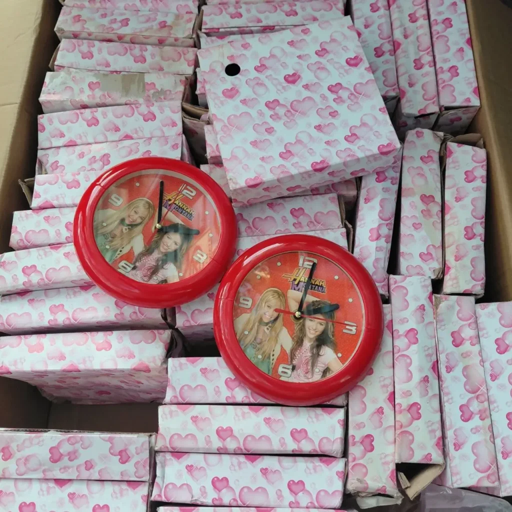 Caja con relojes redondos rojos de Hannah Montana y paquetes envueltos en papel de corazones rosas. by Remates Narvaja