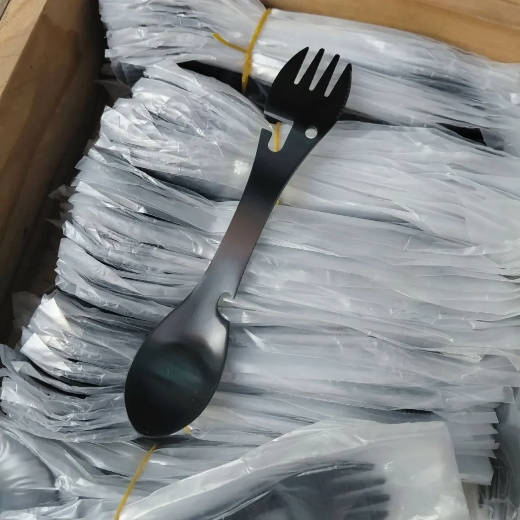 Spork multiherramienta negro sobre un montón de sporks empaquetados. by Remates Narvaja