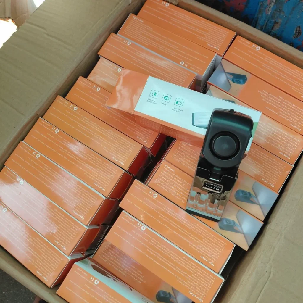 Caja de cartón llena de múltiples alarmas de tope de puerta en sus empaques naranjas. by Remates Narvaja