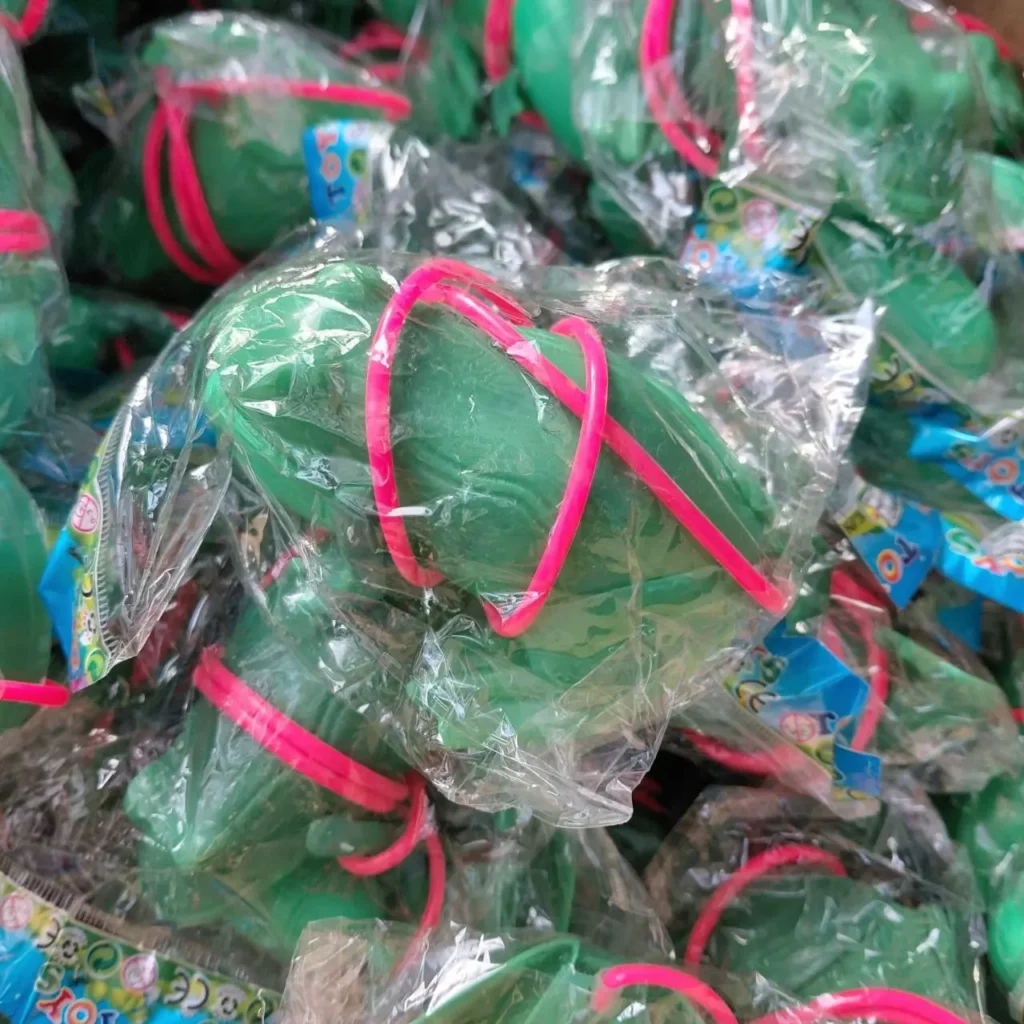 Montón de pequeños juguetes verdes envueltos individualmente en plástico transparente, cada uno con un lazo rosa brillante. by Remates Narvaja
