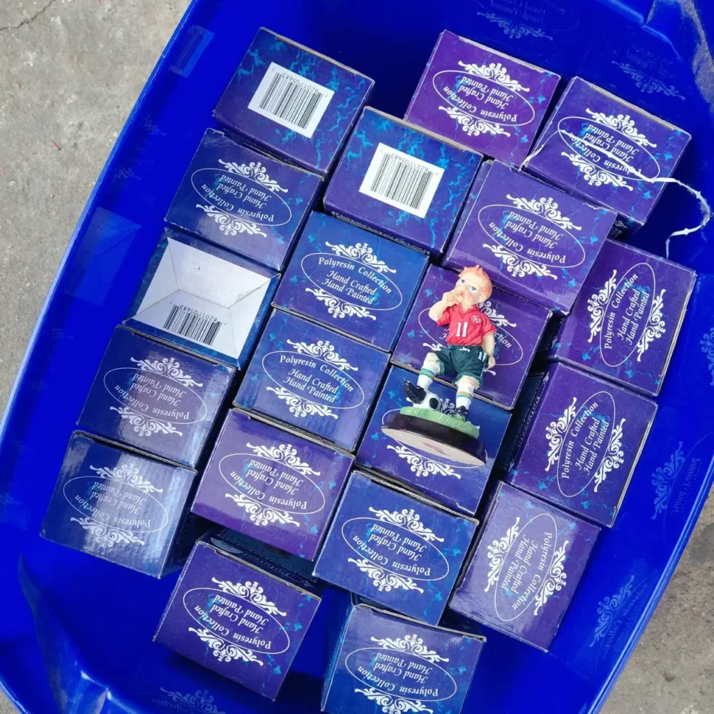 Cajas de colección de figuras de poliresina pintadas a mano en un contenedor azul, con una figura de futbolista visible. by Remates Narvaja