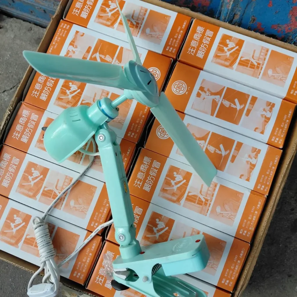 Ventilador de clip de dos aspas color verde menta con cable blanco, sobre una pila de cajas de producto naranjas. by Remates Narvaja