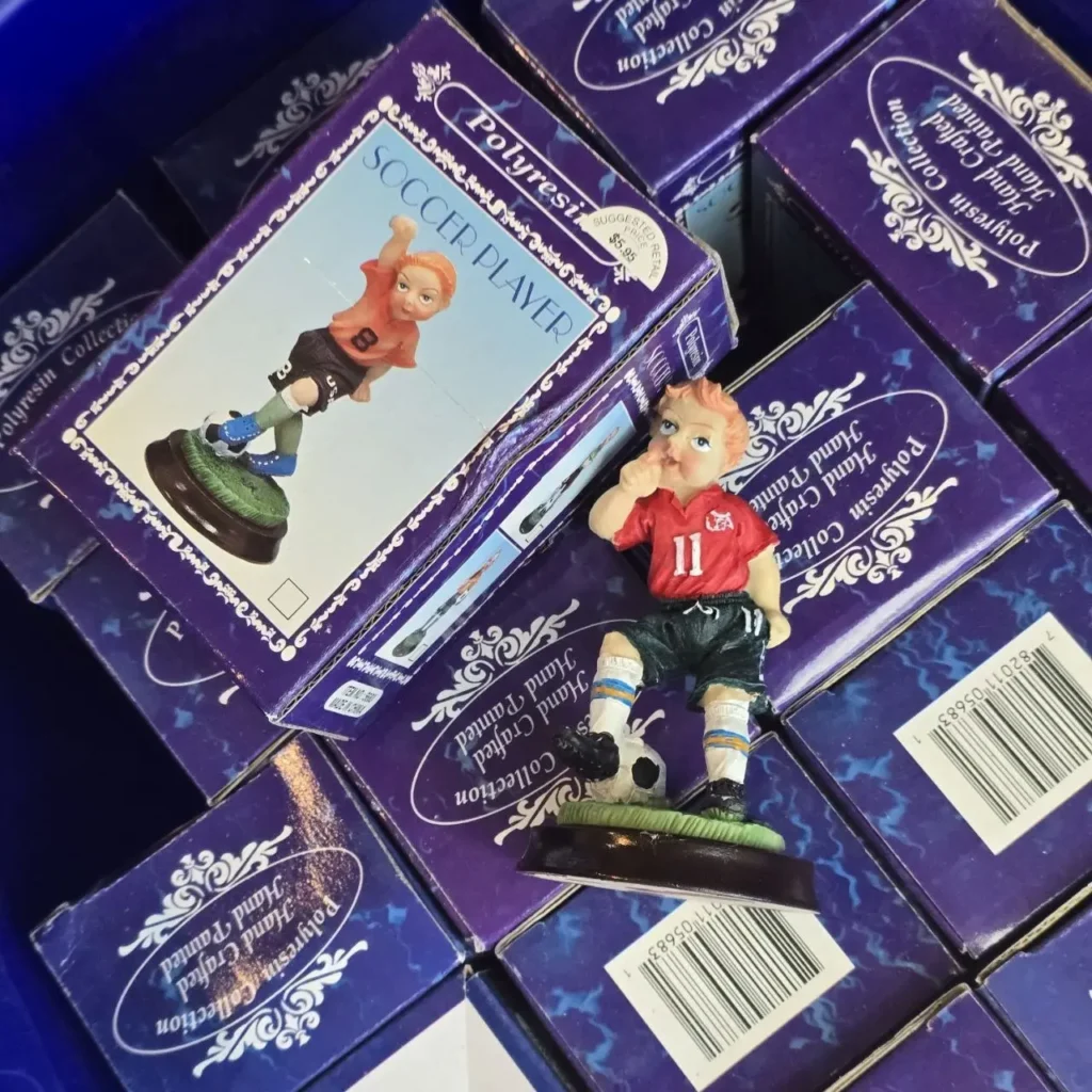 Figuras de jugador de fútbol de poliresina pintadas a mano en cajas moradas, con una figura de niño en camiseta roja y balón de fútbol by Remates Narvaja