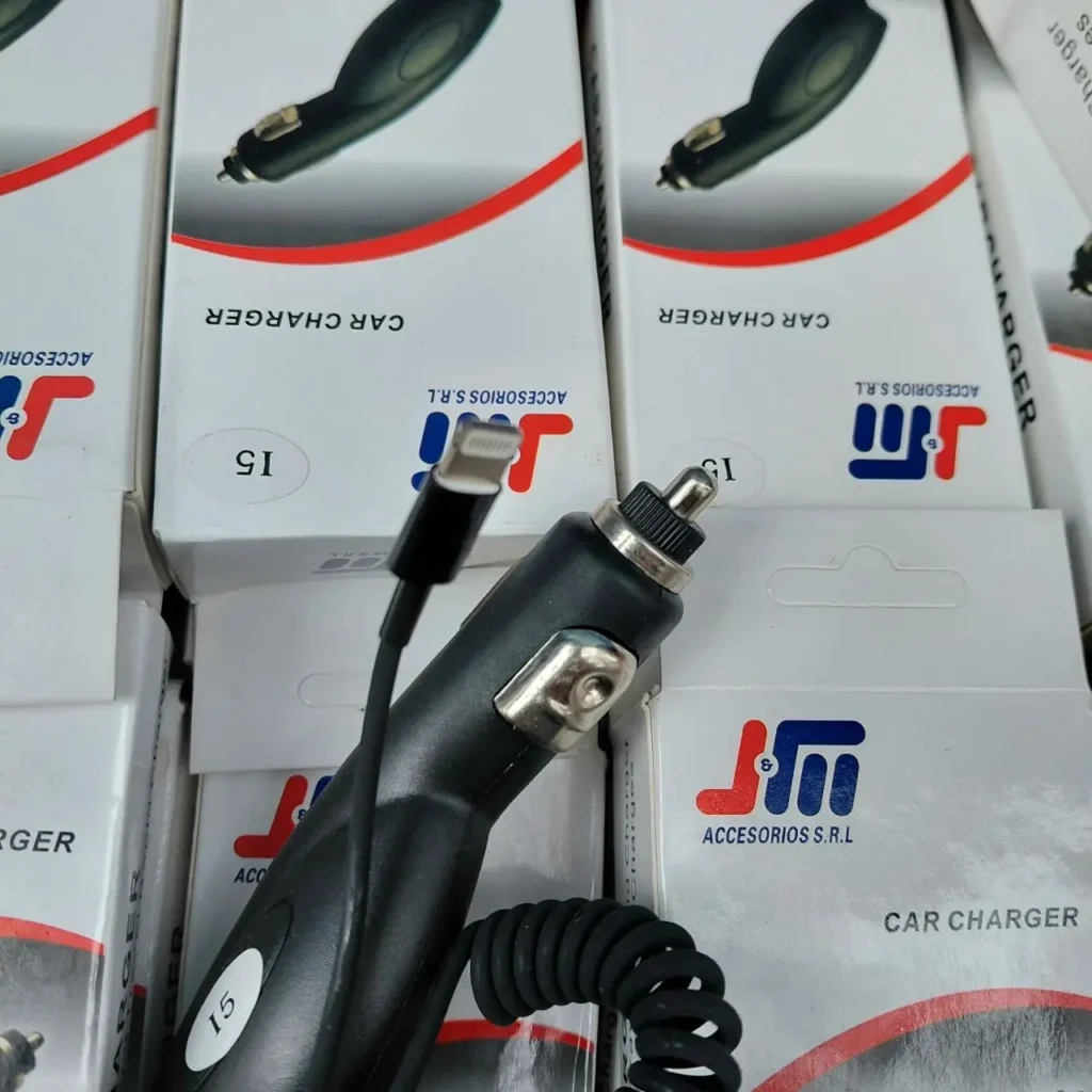 Cargador de coche negro con conector Lightning y cable en espiral, sobre cajas de producto JM. by Remates Narvaja