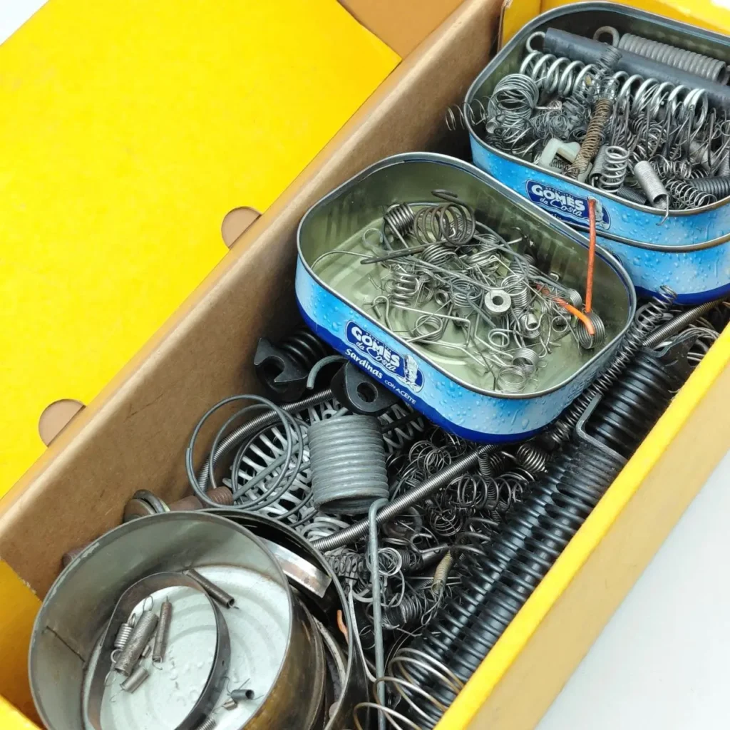 Caja con resortes y piezas metálicas surtidas, organizadas en latas de sardinas. by Remates Narvaja
