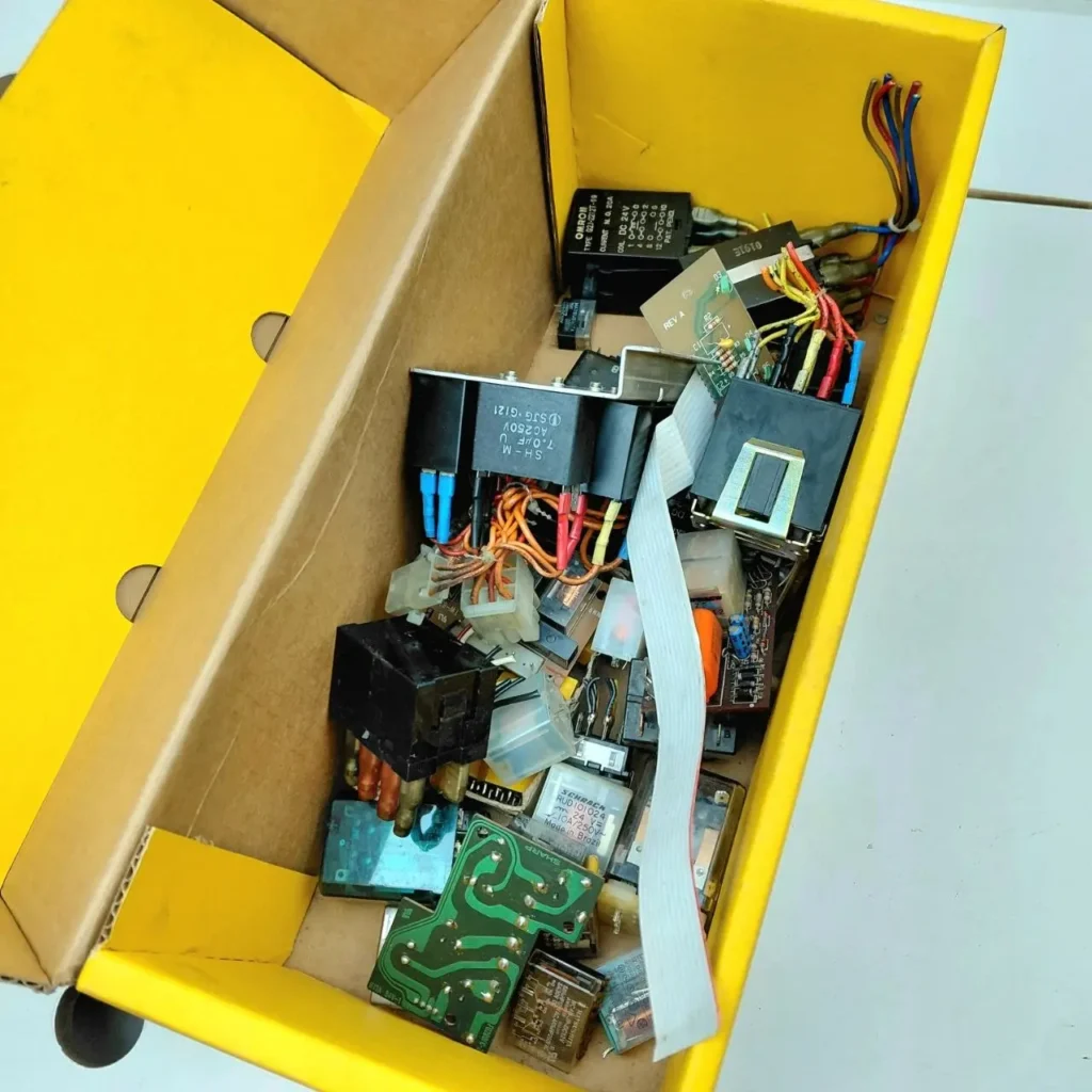 Surtido de componentes electrónicos, relés y placas de circuito en una caja amarilla. by Remates Narvaja
