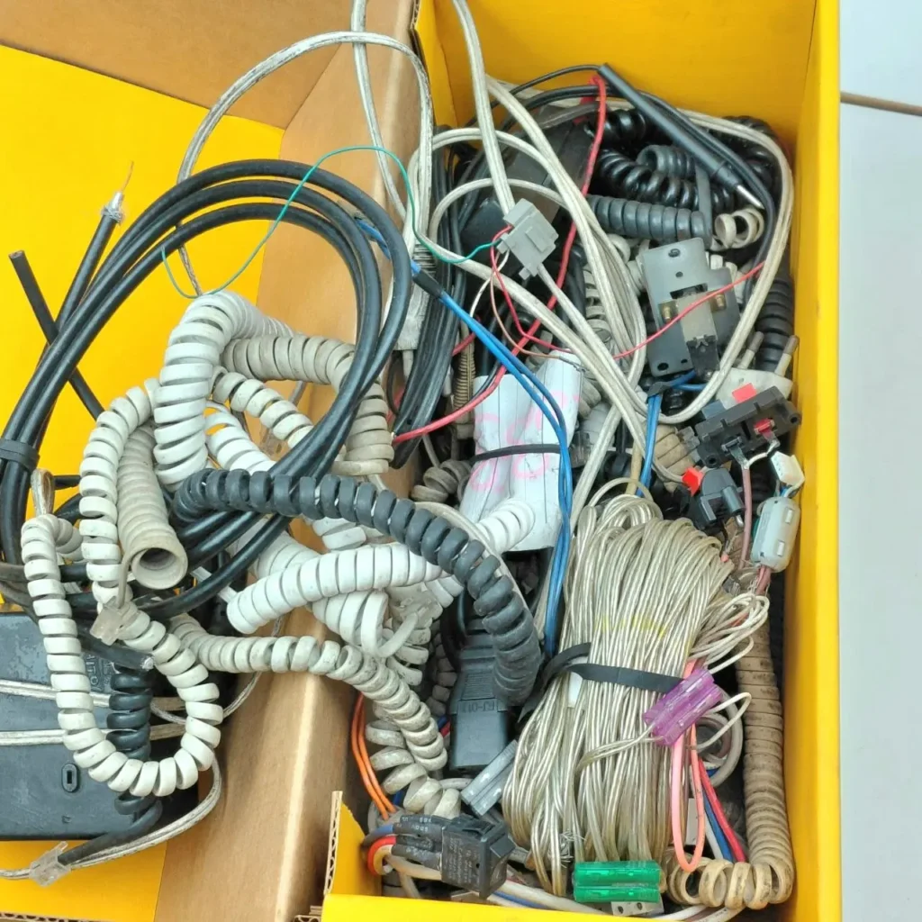 Caja amarilla llena de cables enredados, conectores y componentes electrónicos variados. by Remates Narvaja