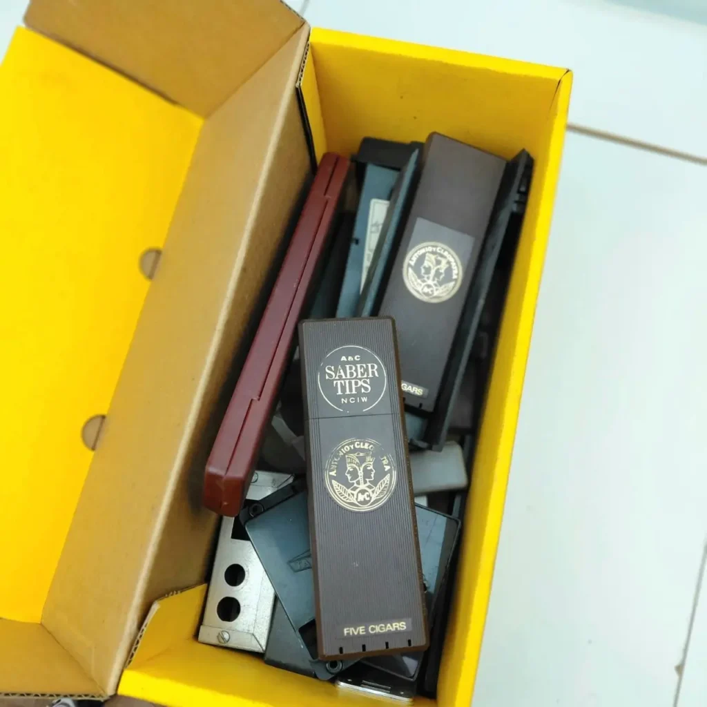Estuches de puros vintage A&C Saber Tips marrones y negros en una caja amarilla. by Remates Narvaja