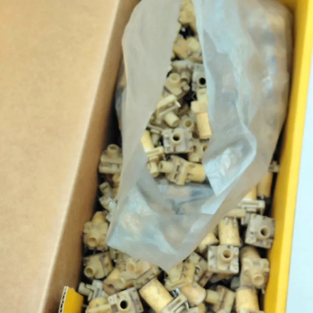 Caja de cartón con pequeñas piezas beige o amarillas, algunas dentro de una bolsa de plástico." by Remates Narvaja