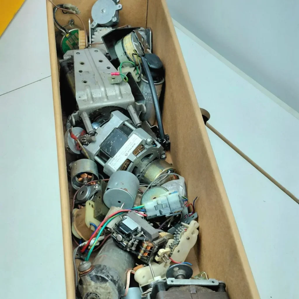 Caja de cartón llena de motores electrónicos usados, engranajes y componentes variados. by Remates Narvaja