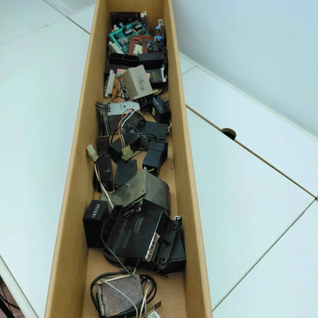 Caja de cartón con componentes electrónicos variados, incluyendo placas de circuito, módulos y un medidor de monedas. by Remates Narvaja
