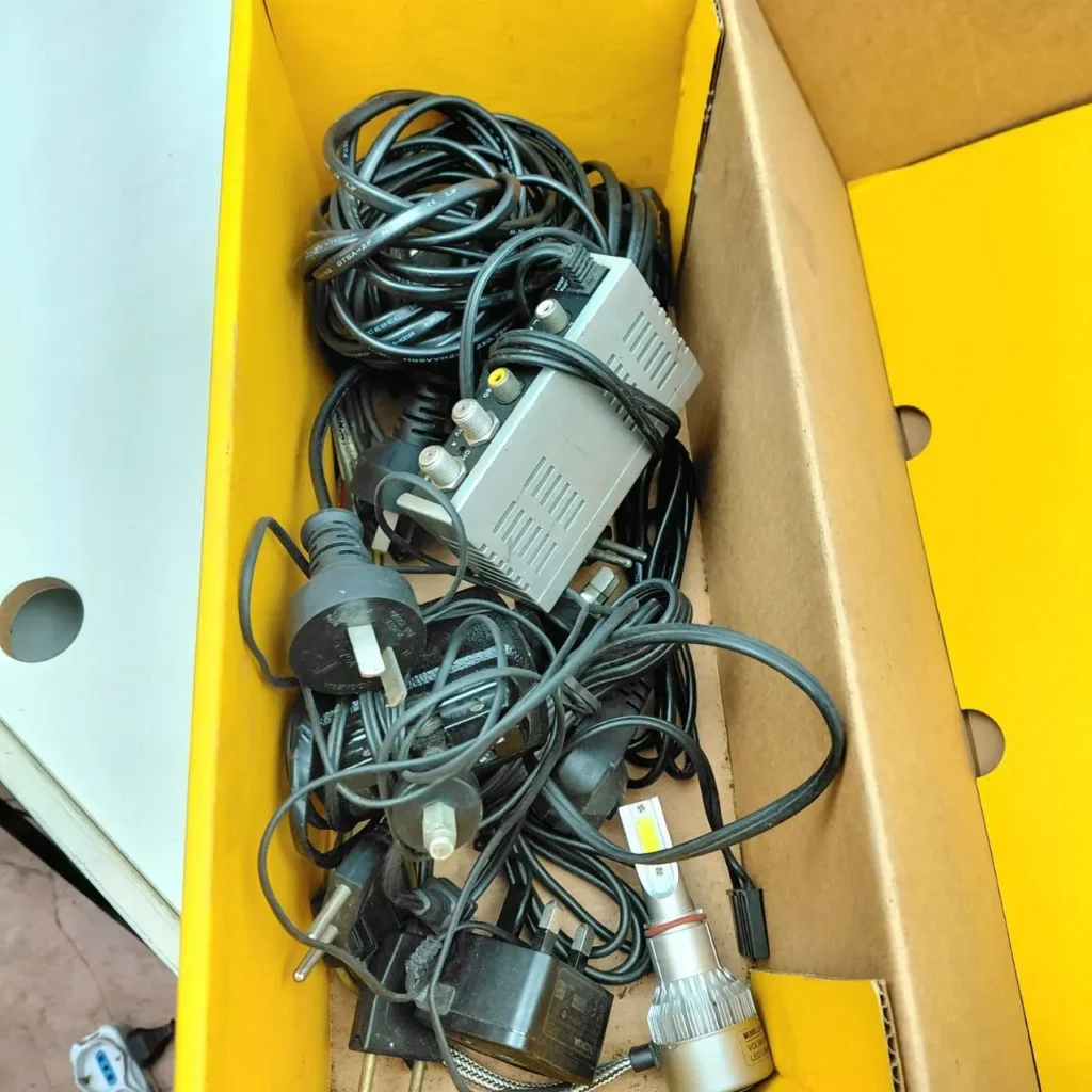 Caja desordenada con cables, adaptadores, un divisor de señal y una bombilla LED. by Remates Narvaja