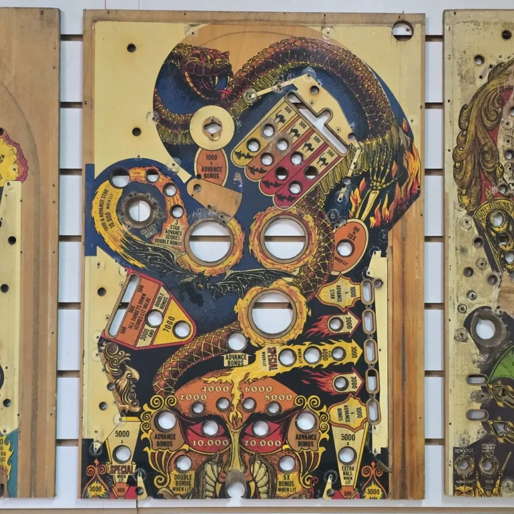 Tablero de juego de pinball vintage desgastado con ilustración de serpiente, llamas y murciélagos. by Remates Narvaja