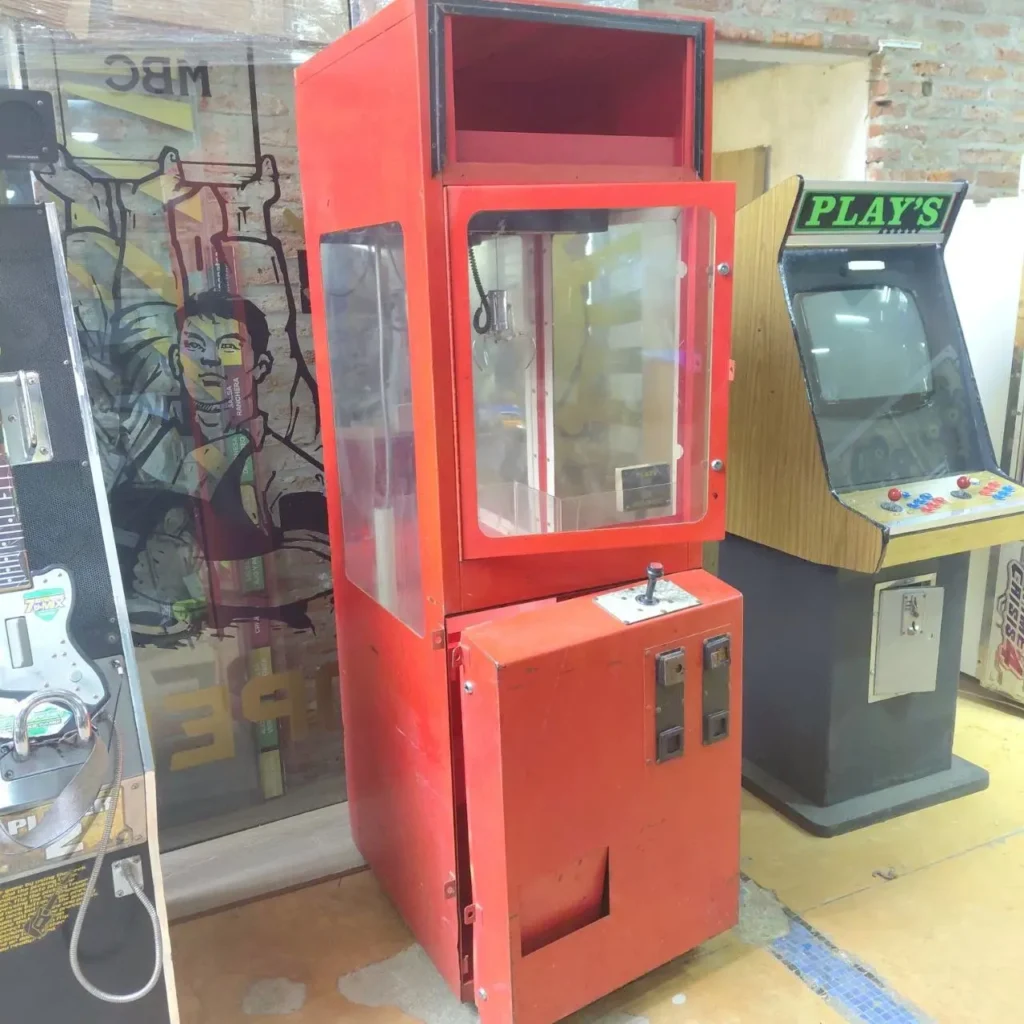 Máquina de gancho roja antigua junto a una máquina de arcade vintage "PLAY'S". by Remates Narvaja
