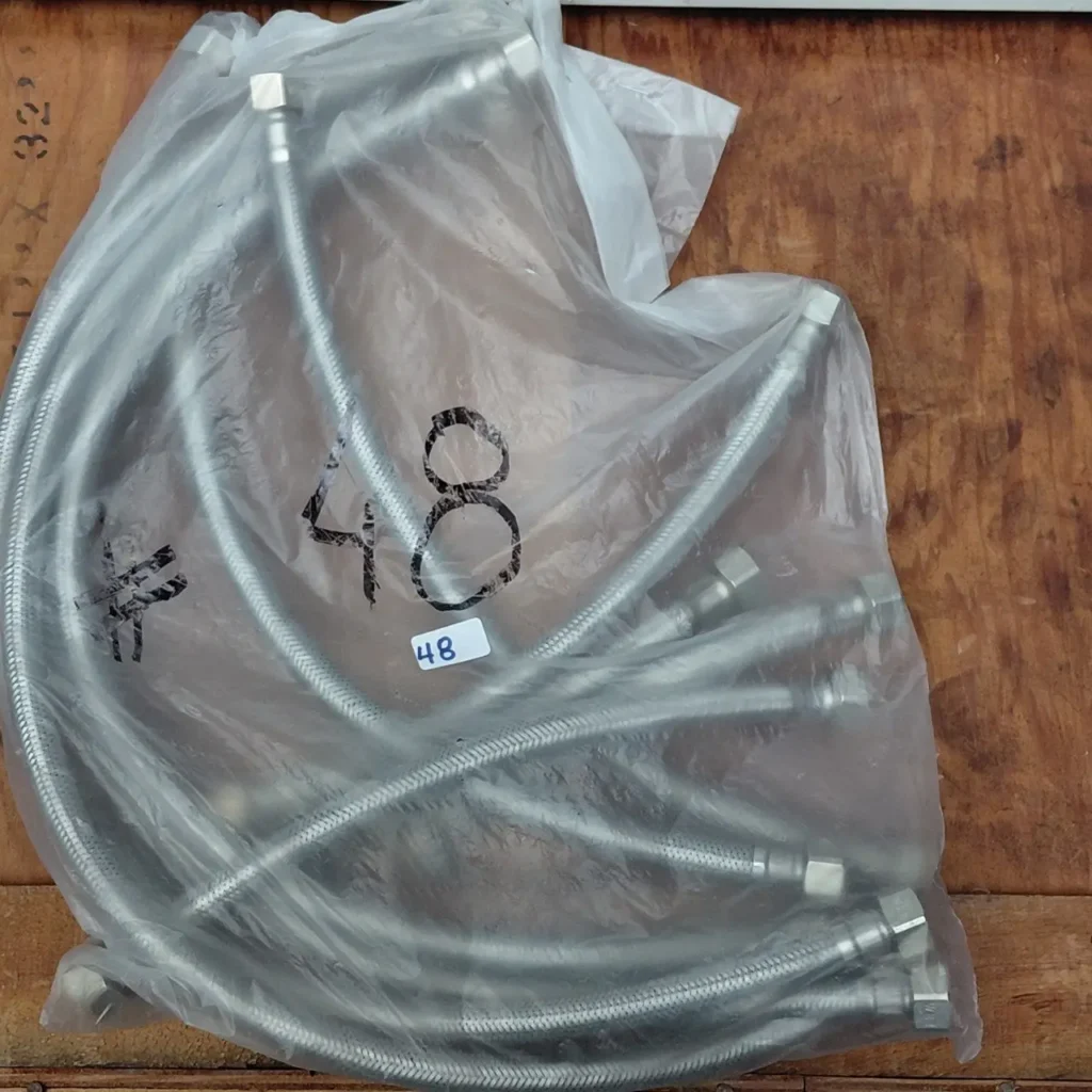 Mangueras flexibles de acero inoxidable trenzado en una bolsa de plástico transparente, con conectores metálicos y el número 48 visible. by Remates Narvaja