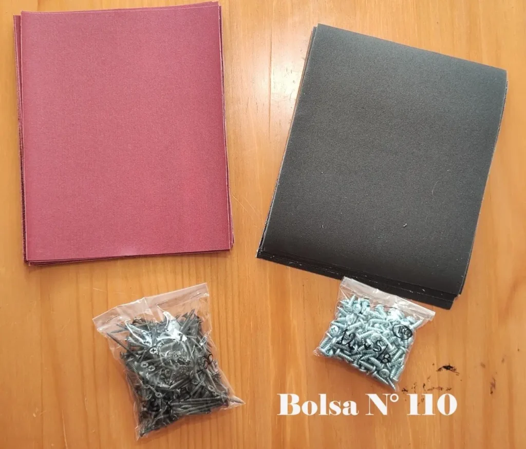 Dos pilas de hojas (rojas y negras) y dos bolsas de tornillos (negros y plateados) sobre una mesa de madera, con by Remates Narvaja