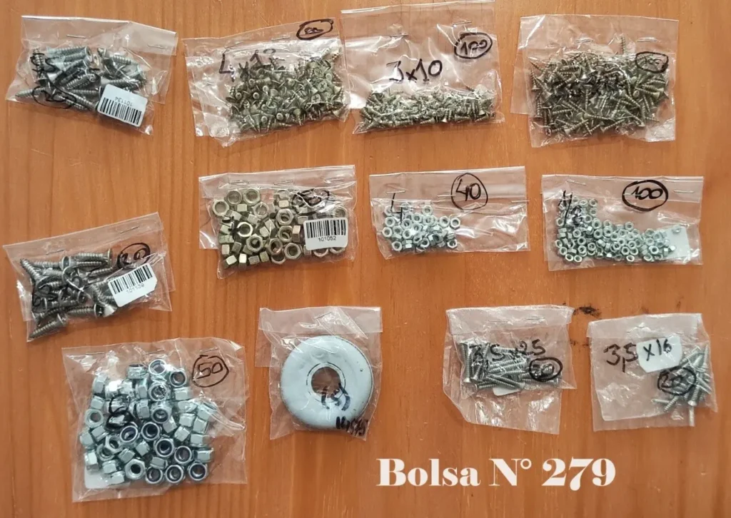 Varias bolsas de tornillos, tuercas y herrajes pequeños sobre madera, etiquetado como Bolsa N° 279. by Remates Narvaja