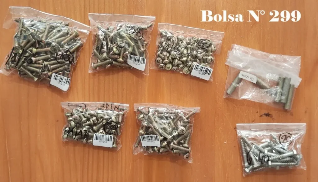 Siete bolsas de tornillos y sujetadores variados sobre una superficie de madera, con la etiqueta "Bolsa N° 299". by Remates Narvaja