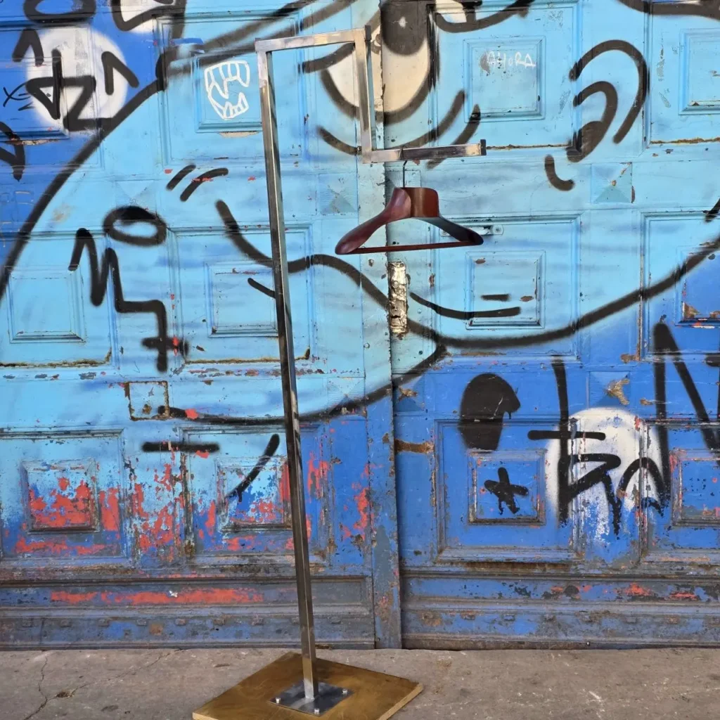 Perchero metálico con percha de madera frente a puerta azul con graffiti. by Remates Narvaja