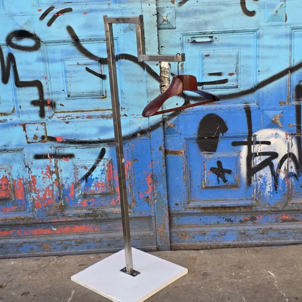 Perchero de ropa metálico con percha de madera frente a puerta azul con grafitis. by Remates Narvaja