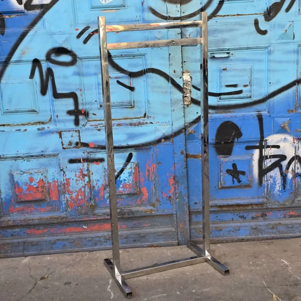 Perchero de metal cromado vacío frente a puerta azul con graffiti. by Remates Narvaja