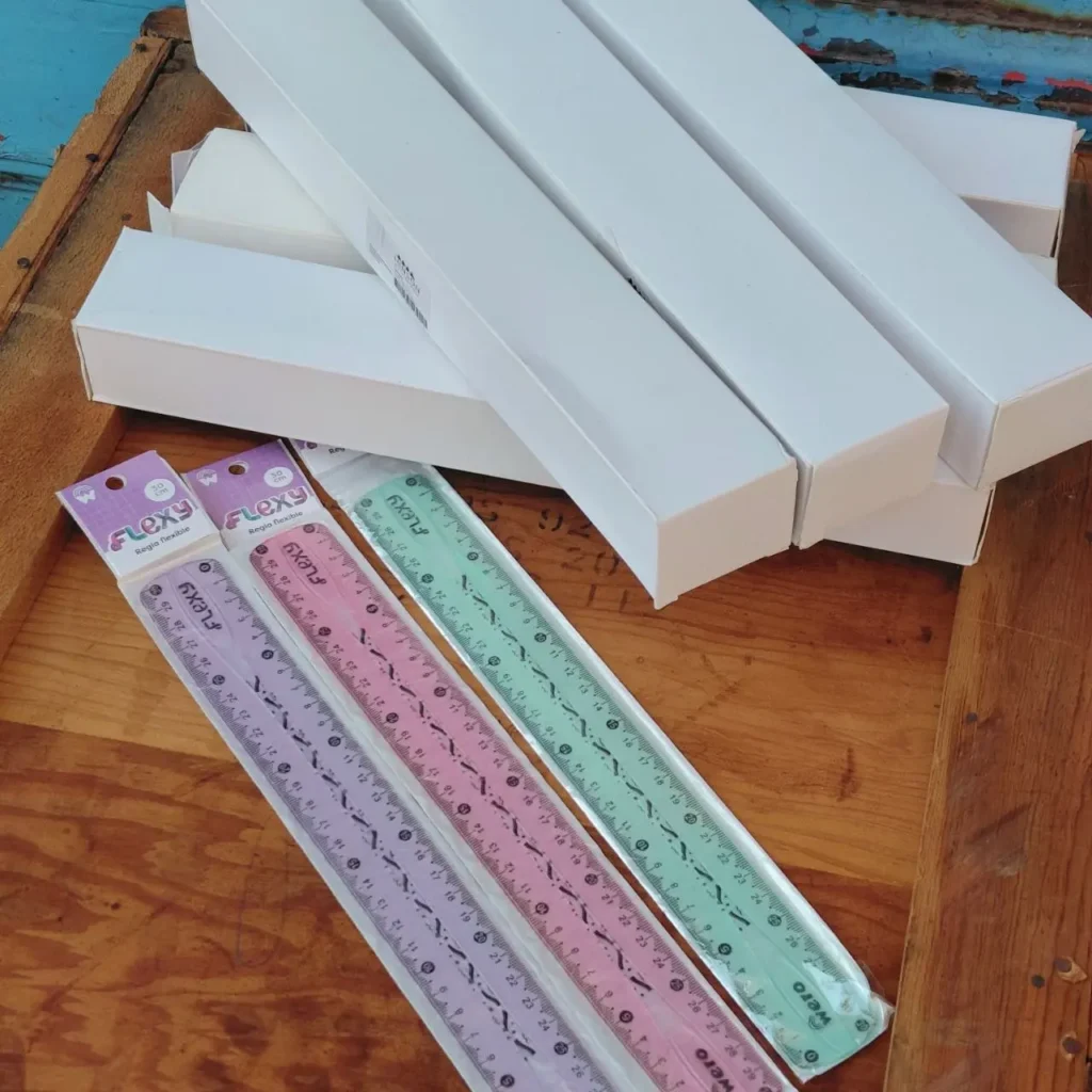 Reglas flexibles Flexy de 30 cm en colores pastel (morado, rosa, verde) junto a cajas blancas de embalaje. by Remates Narvaja