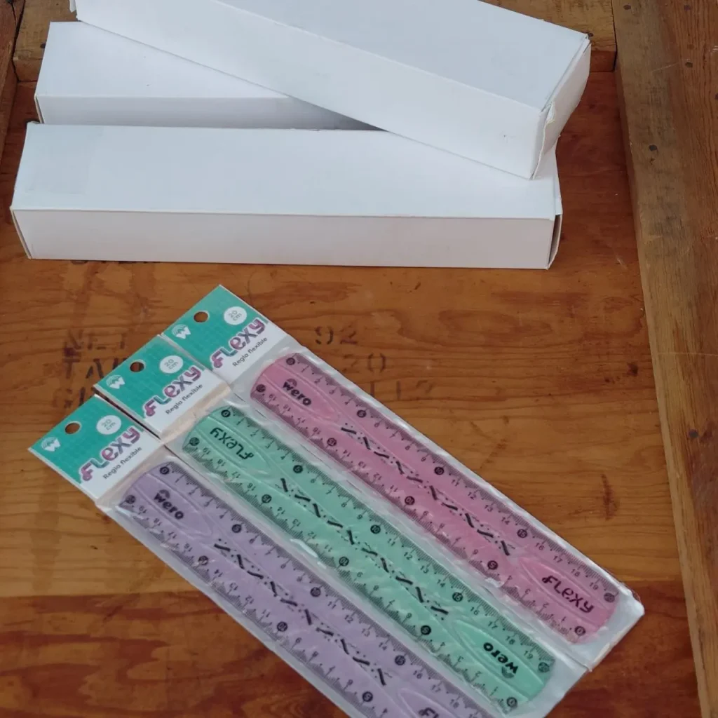 Reglas flexibles Flexy Wero de 20 cm en colores rosa, verde y morado, empaquetadas sobre una mesa de madera con cajas blancas al fondo. by Remates Narvaja