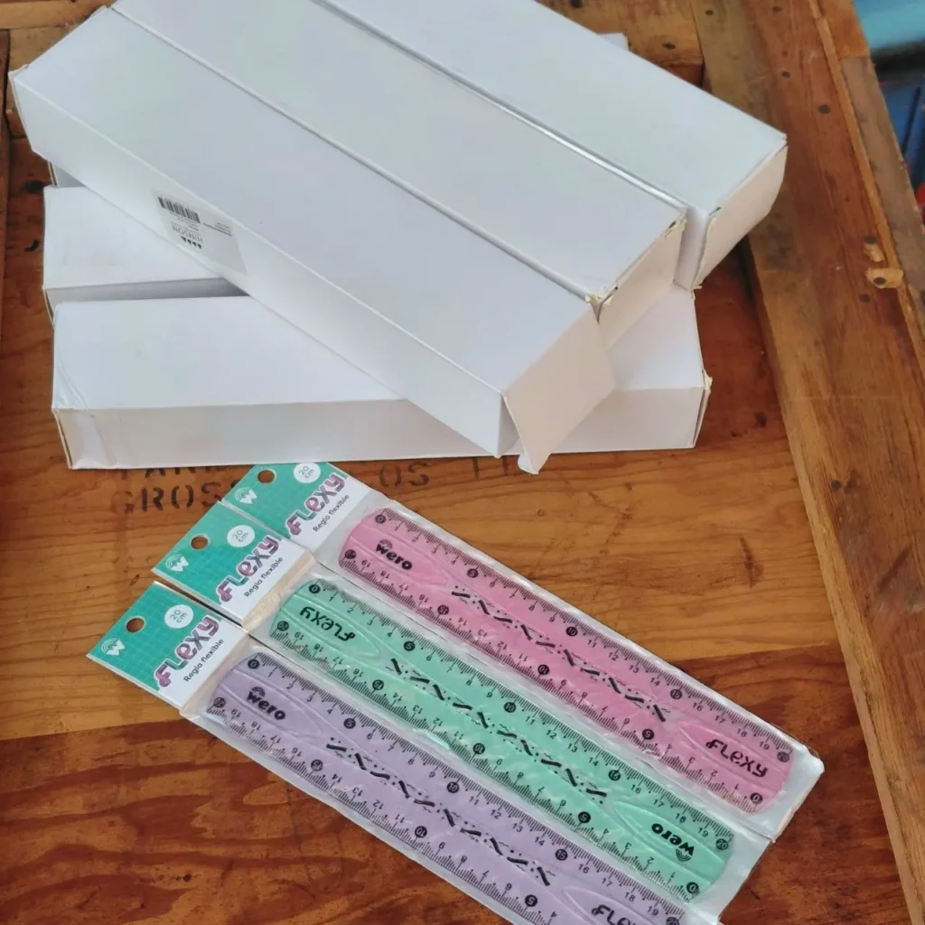 Reglas flexibles Flexy Wero de 20 cm en colores rosa, verde y morado, con cajas blancas apiladas en el fondo sobre una superficie de madera. by Remates Narvaja