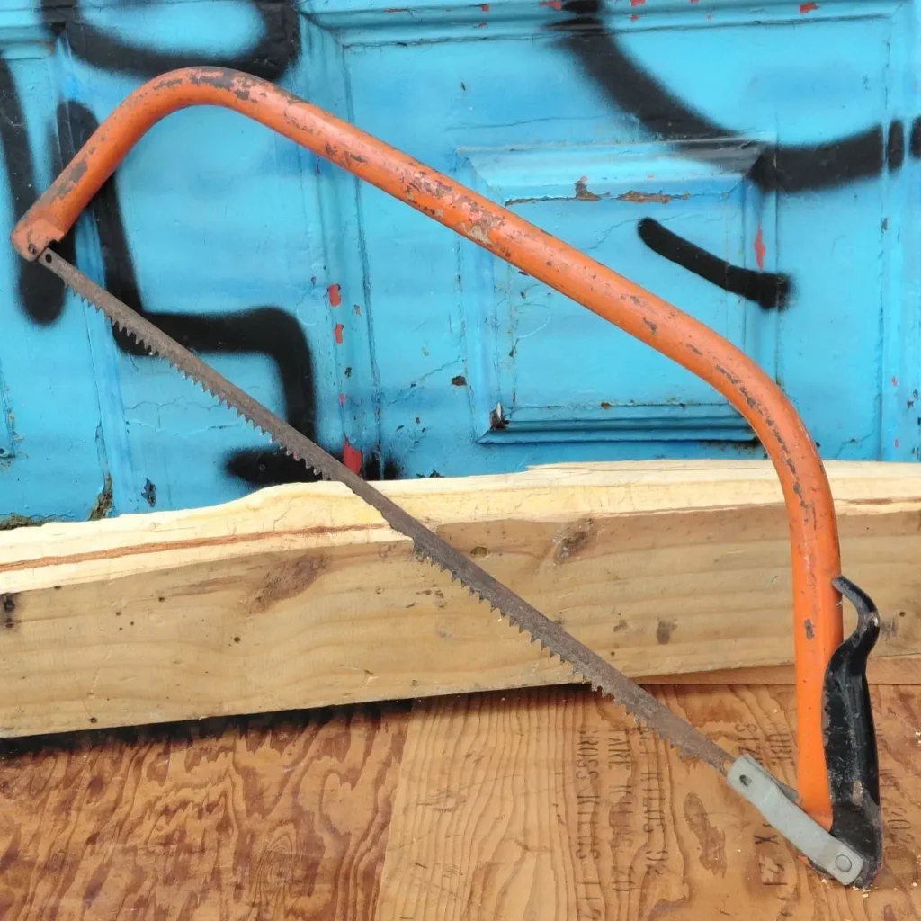 Serrucho de arco naranja oxidado sobre tabla de madera. by Remates Narvaja