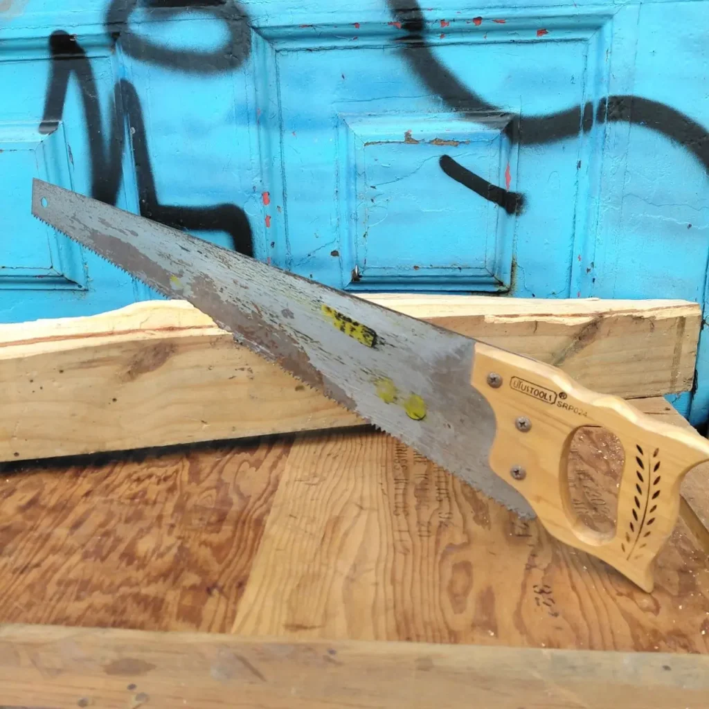 Sierra de mano con mango de madera sobre tablas de madera, fondo azul. by Remates Narvaja
