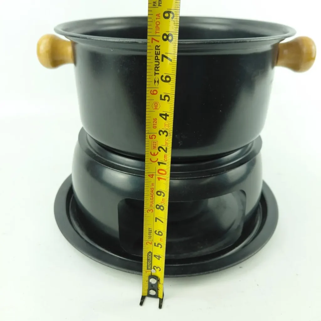 Olla de fondue negra con asas de madera y base, mostrando su altura con una cinta métrica. by Remates Narvaja