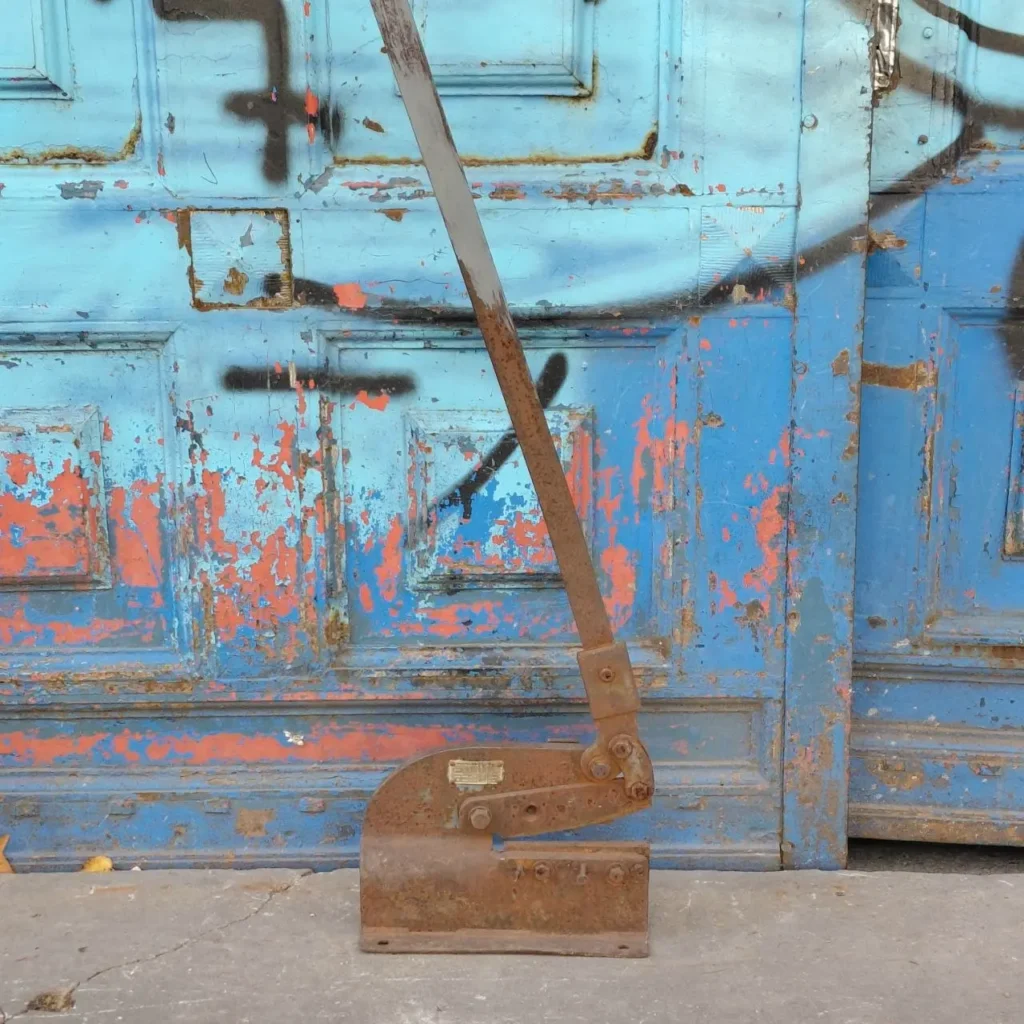 Cizalla manual oxidada frente a una puerta azul desgastada. by Remates Narvaja